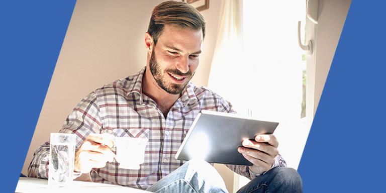 Bearded man sips tea while using Bill Pay to pay his bills on a tablet