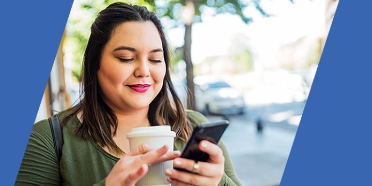 Woman looking at her phone while holding a coffee